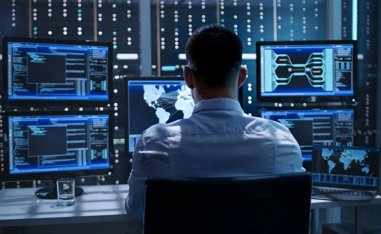 A man sitting in front of multiple computer screens.